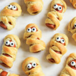 Mummy Hot Dogs served on a white marble tray.