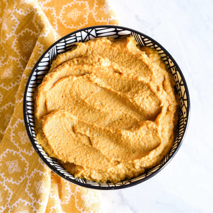 A bowl of Pumpkin Hummus served next to a yellow napkin.
