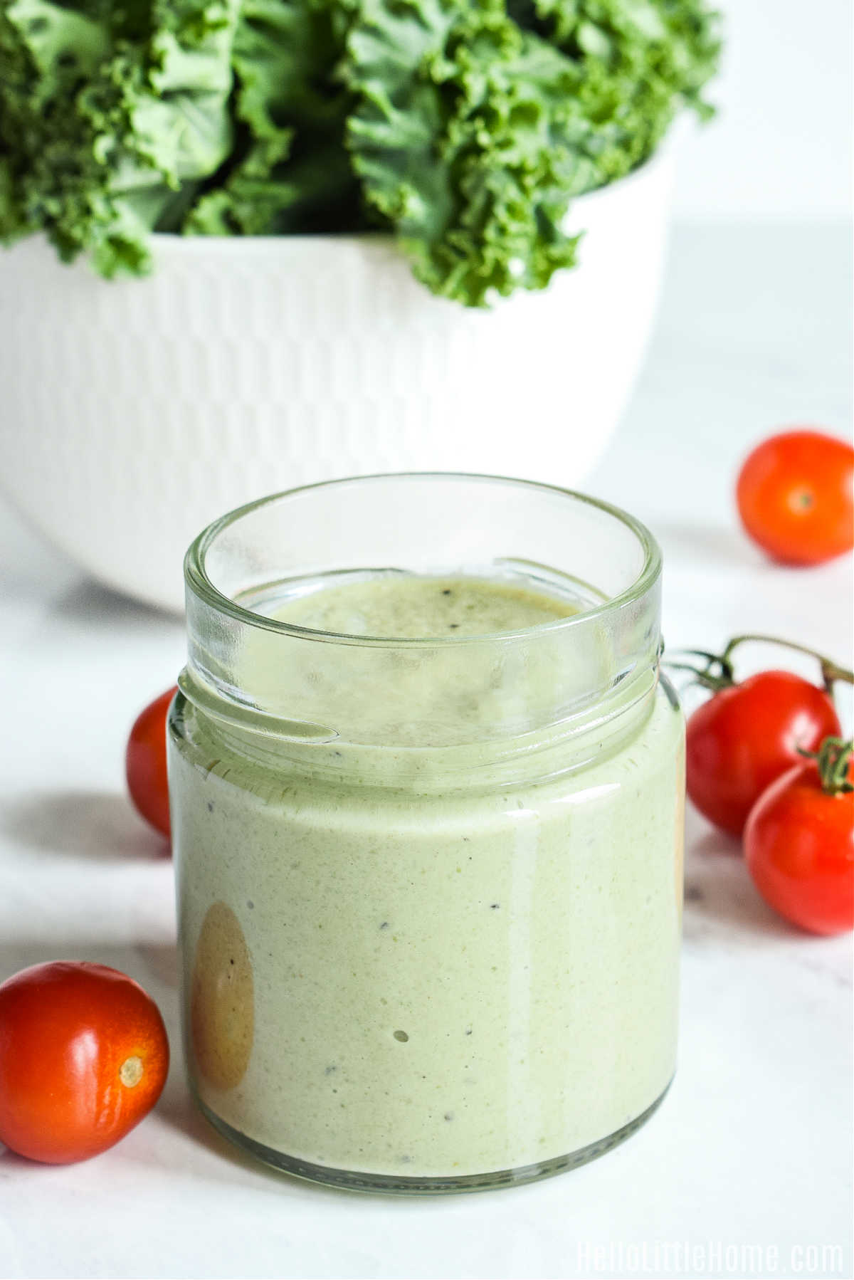 The finished dressing, tomatoes, and kale on a marble counter.