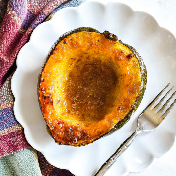 One of the Roasted Acorn Squash Halves served on a white plate with a fork.
