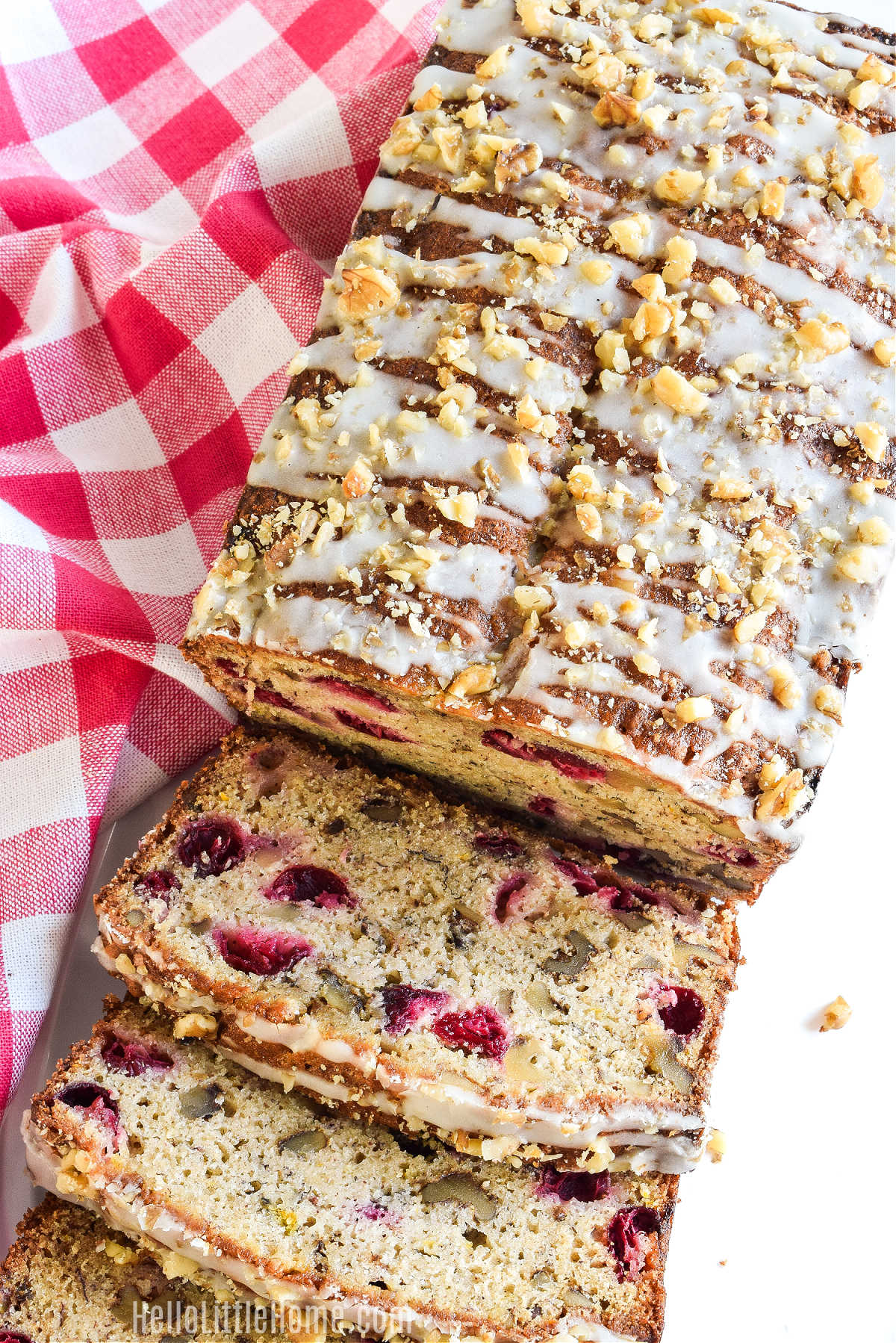 A quick bread drizzled with glaze and sprinkled with nuts served with a checked napkin.