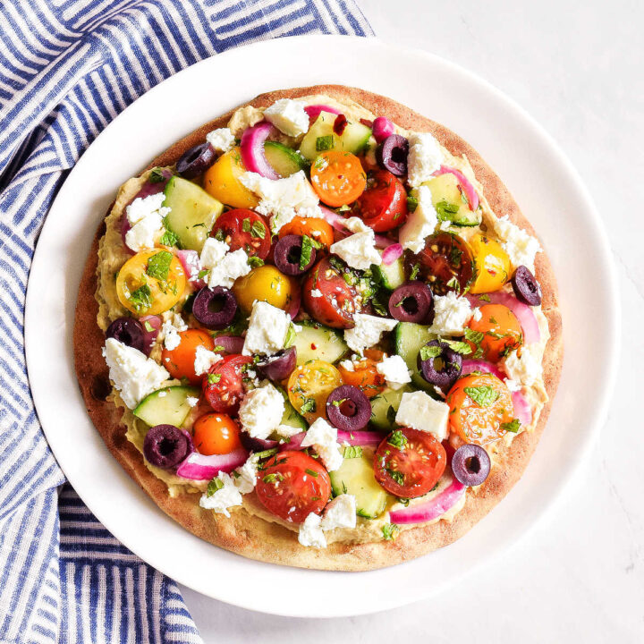 A Hummus Pita topped with veggies, feta, and olives on a white plate.