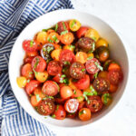 Marinated Tomatoes served in a white bowl next to a striped napkin.