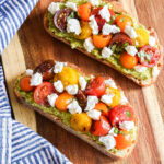 Homemade Pesto Ricotta Toast with Tomatoes on a wood board.