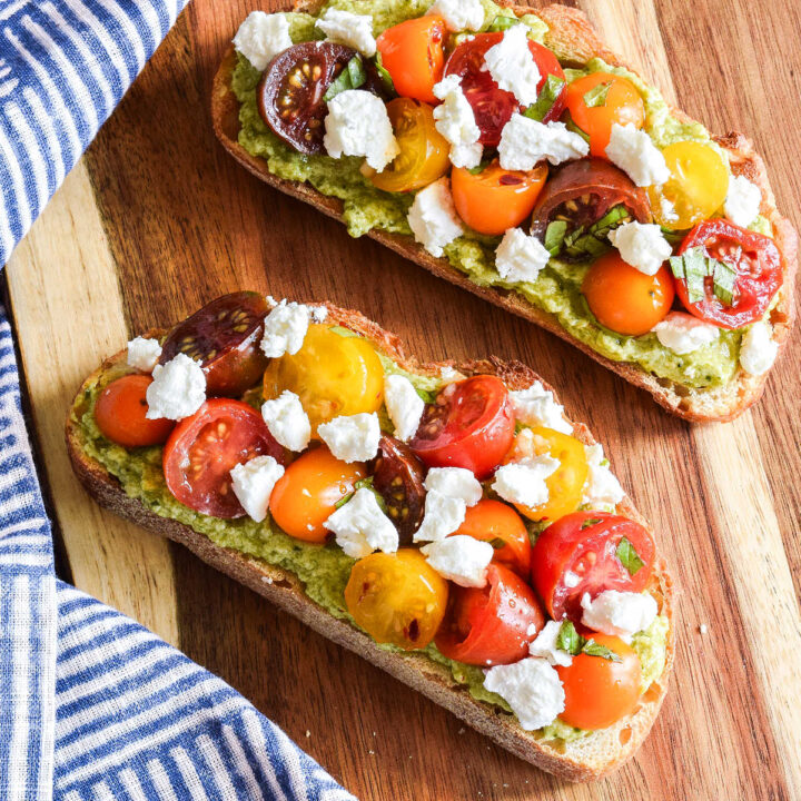 Homemade Pesto Ricotta Toast with Tomatoes on a wood board.