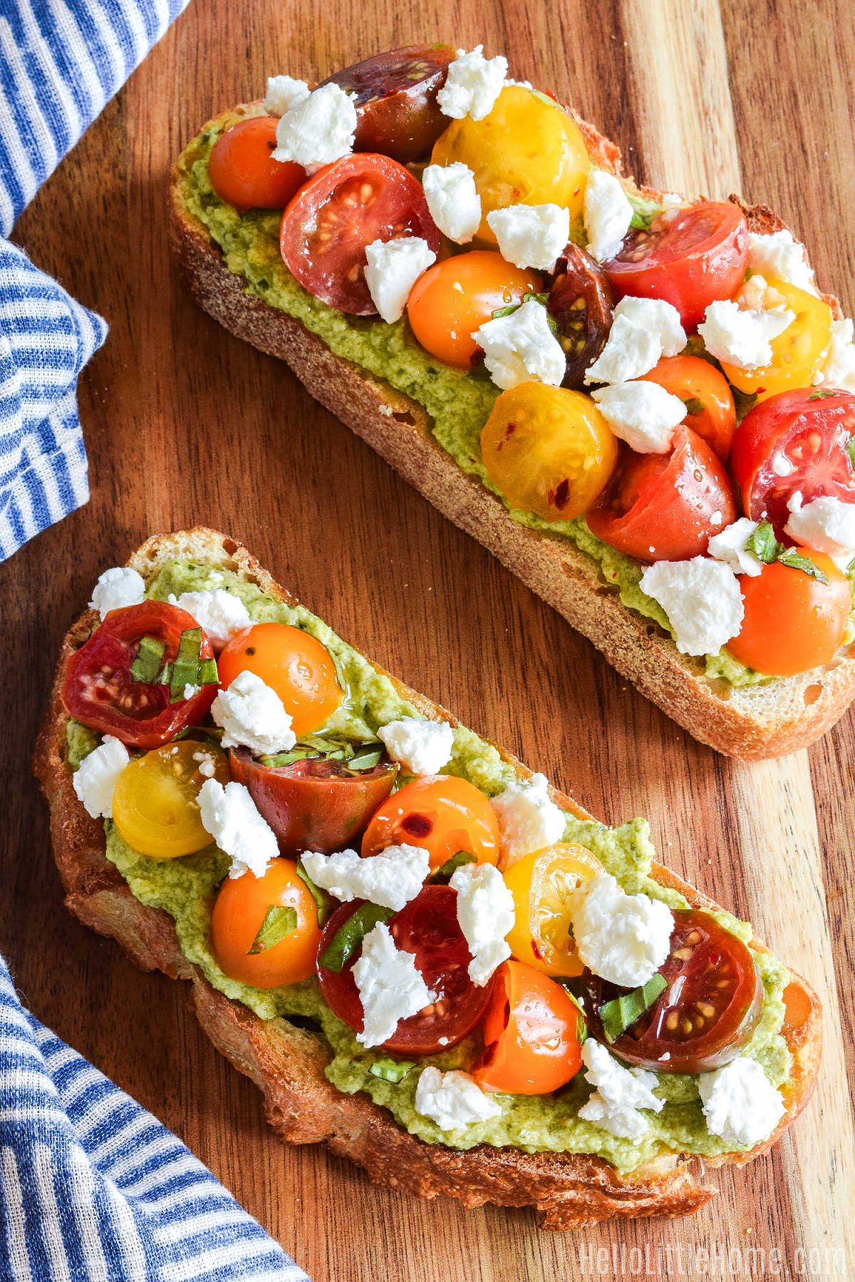 Slices of Pesto Ricotta Toast topped with Tomatoes and Goat Cheese on a wood board.