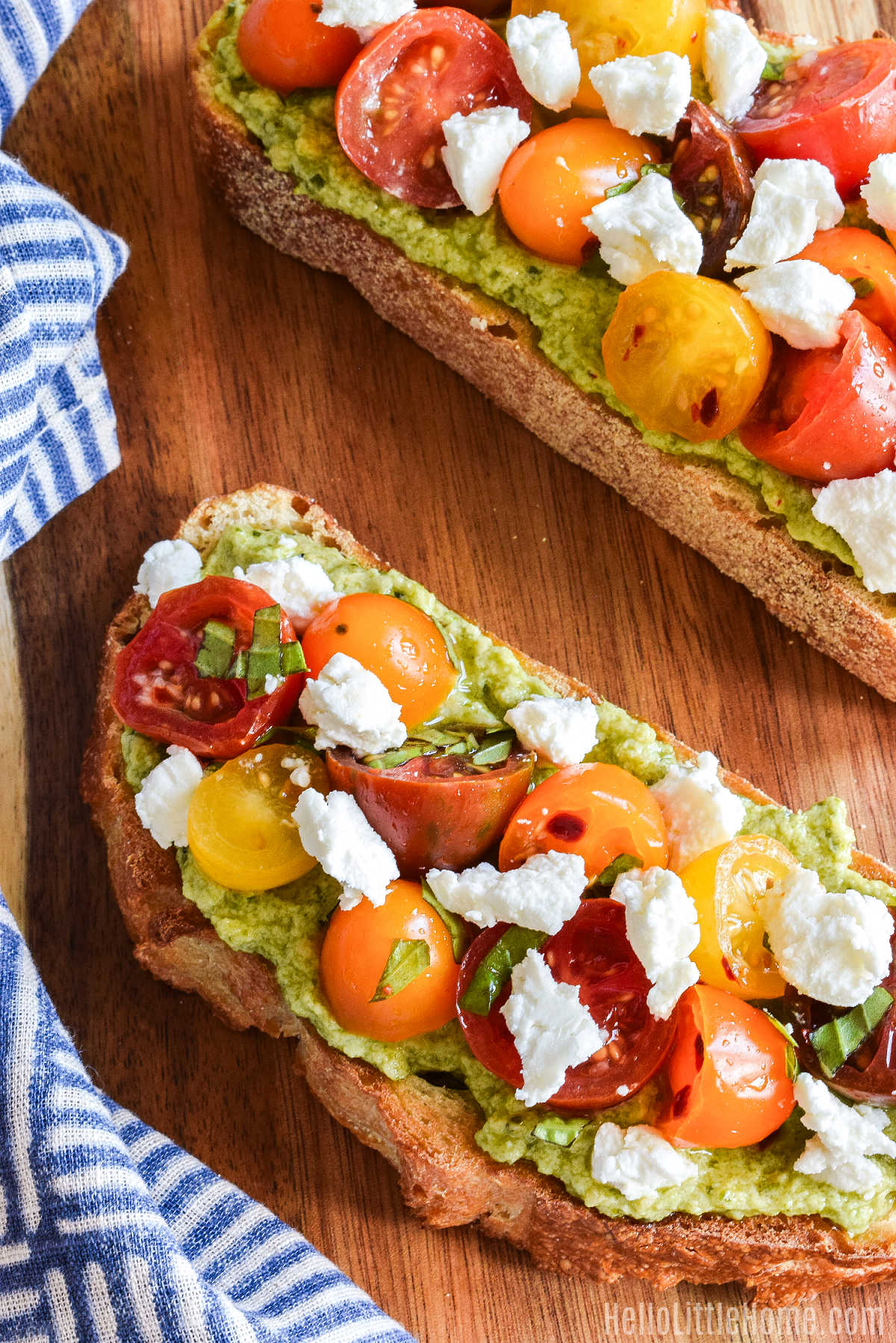 Slices of Ricotta Cheese Toast with pesto and tomatoes served on a wood board.