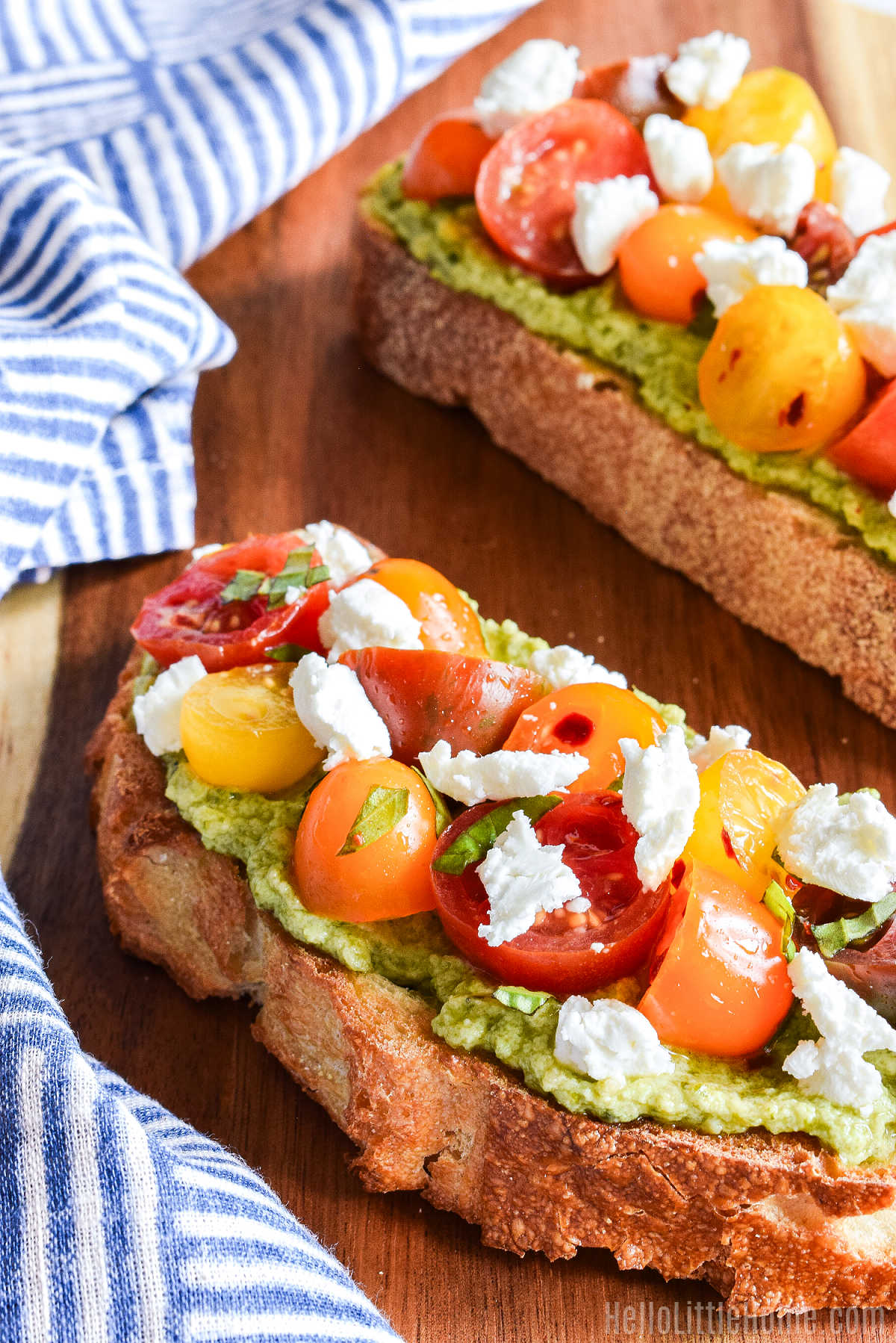 Two slices of Pesto Ricotta Toast served on a wood board with a striped napkin.