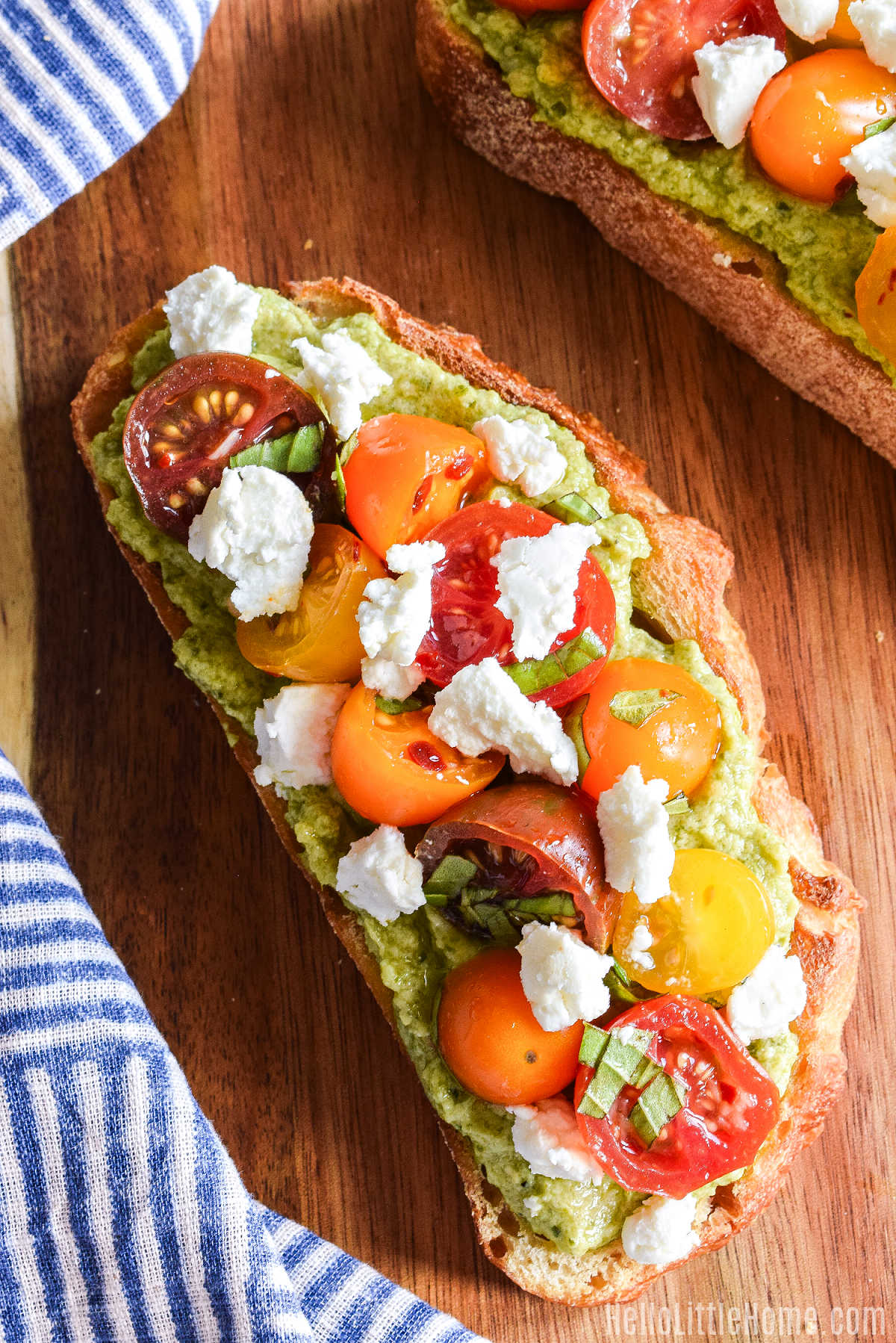 Closeup of a slice of sourdough toast topped with pesto, tomatoes, and cheese.