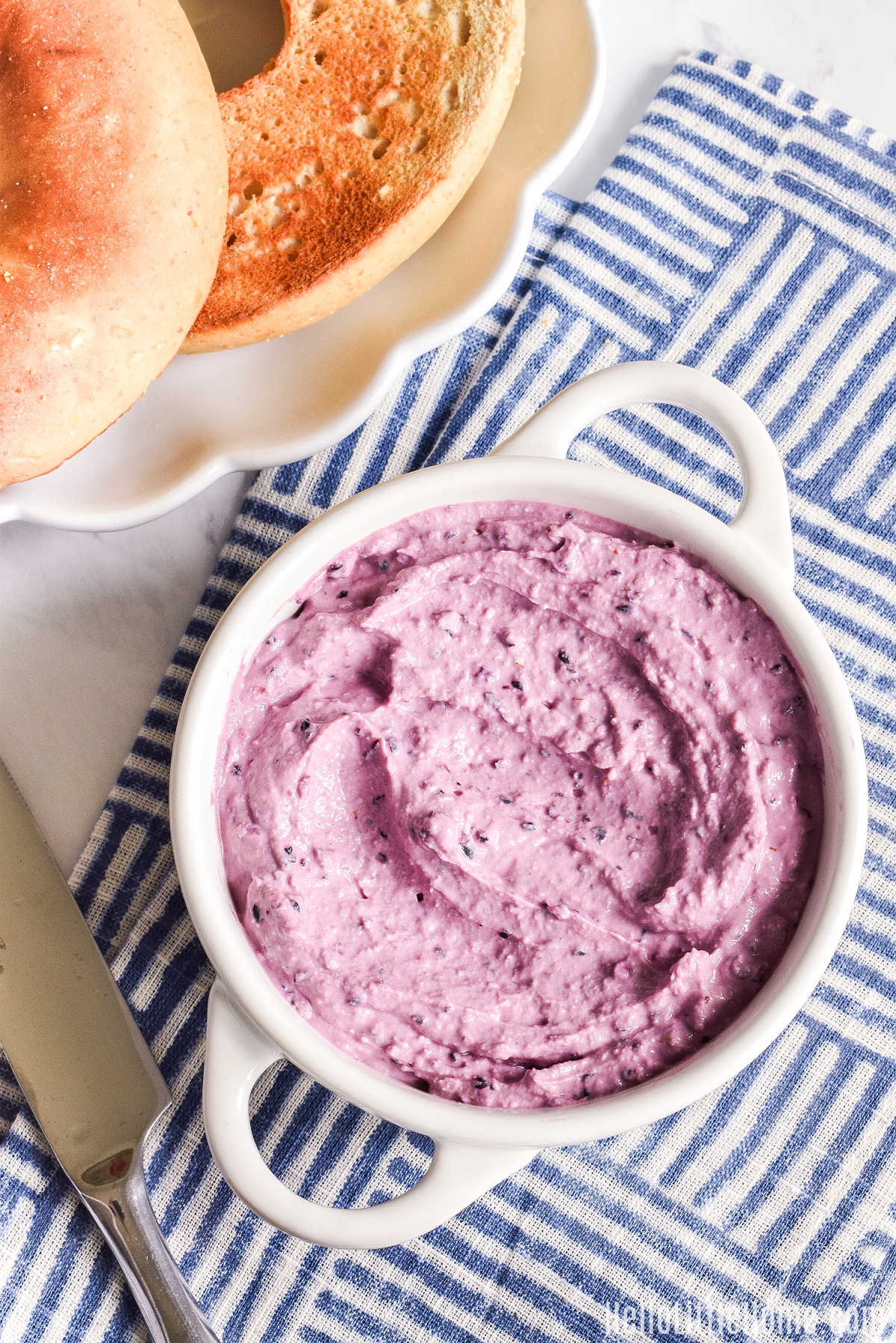 A container of the blueberries and cream cheese recipe next to a plate of bagels.