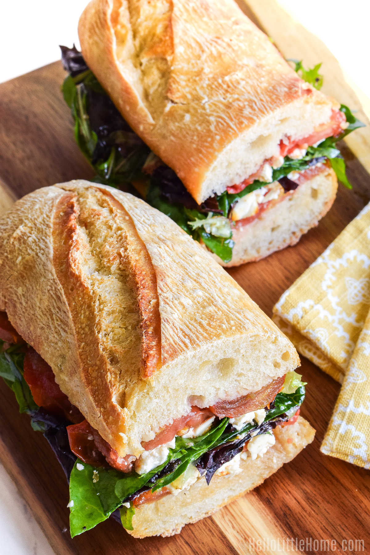 Two sandwich halves and a yellow napkin on a wood cutting board.