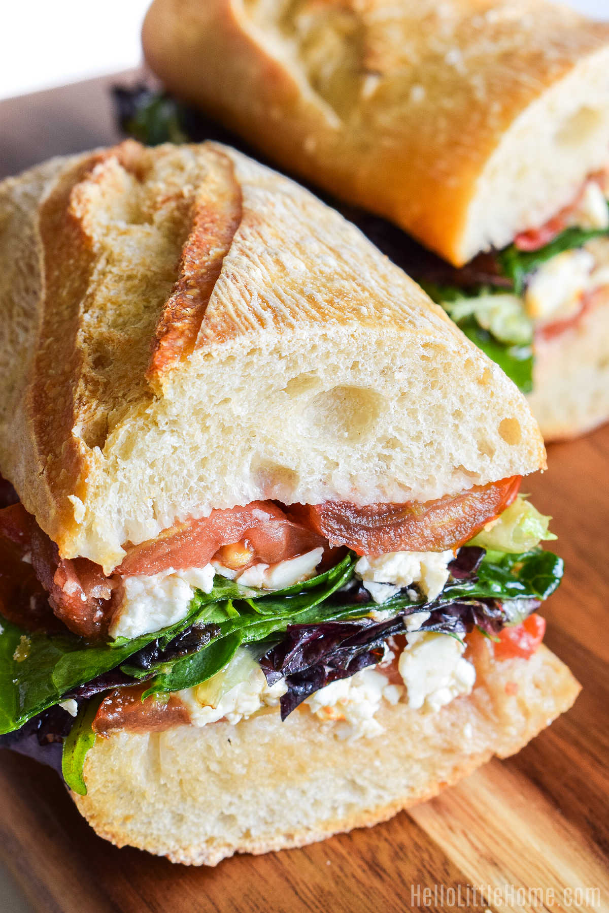 Two halves of a Feta Sandwich on a wood cutting board.