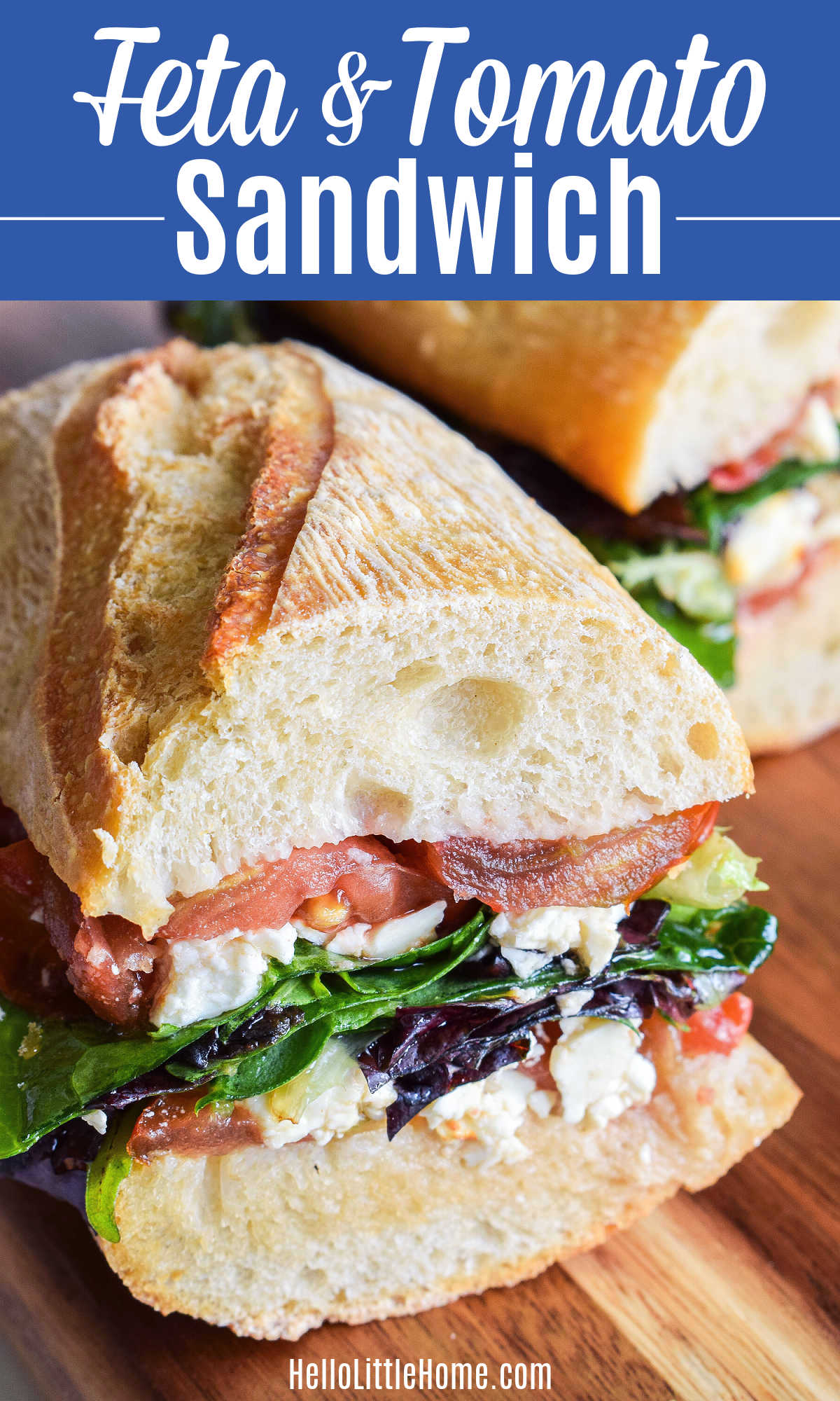 Closeup of a Feta Sandwich with tomatoes and mixed greens served on a wood board.