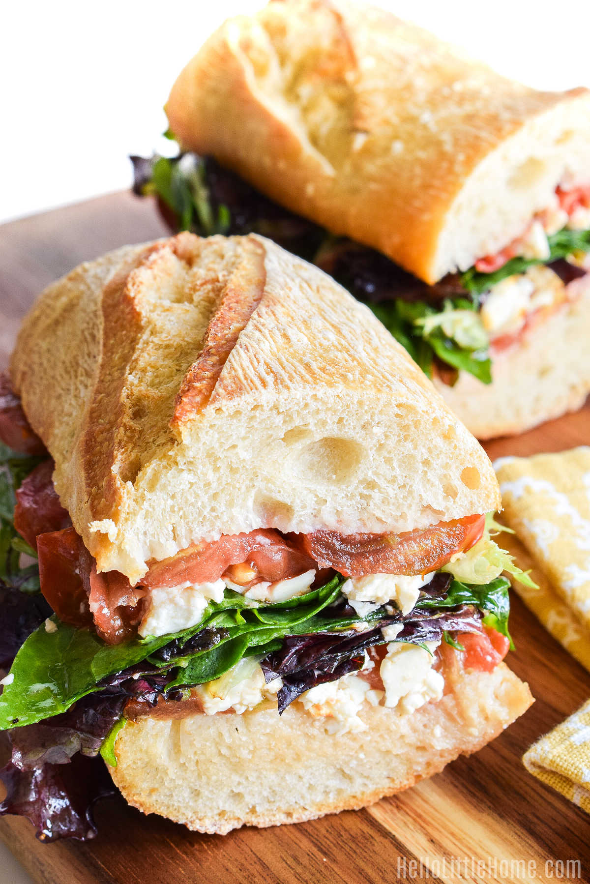 Two halves of a Baguette Feta Tomato Sandwich on a wood cutting board.