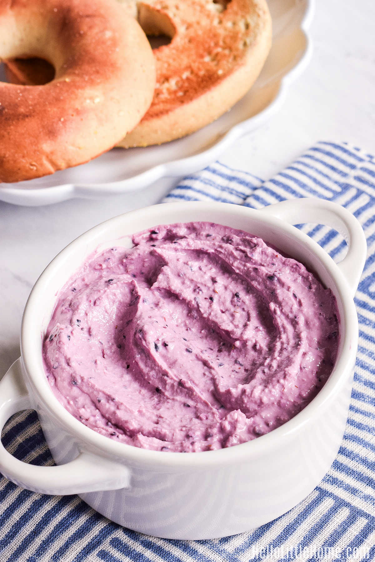 A container of the flavored cream cheese next to a plate of bagels.