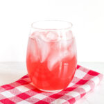 A glass of Watermelon Soda and a checked napkin on a marble counter.