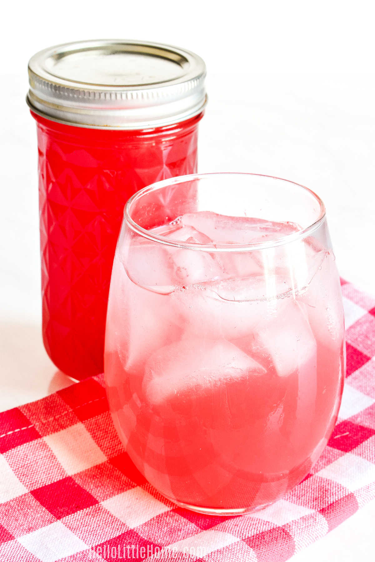 A glass of the finished drink in front of a jar of watermelon syrup.