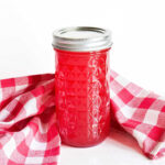 A jar of Watermelon Syrup and a checked napkin on a marble counter.