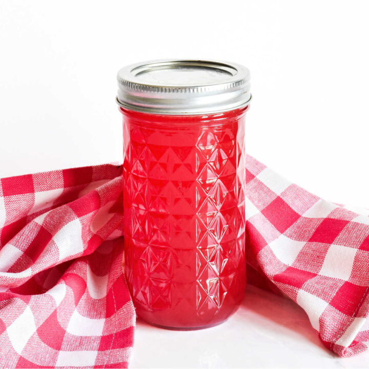 A jar of Watermelon Syrup and a checked napkin on a marble counter.