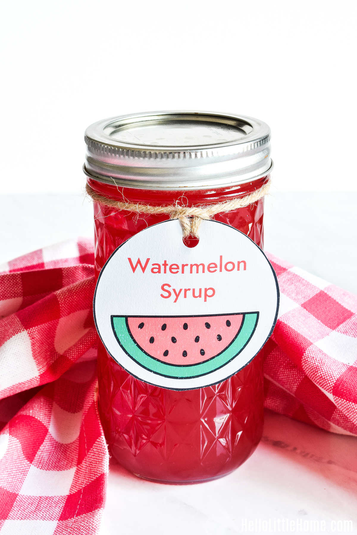 Homemade Watermelon Syrup in a jar decorated with on a marble counter.
