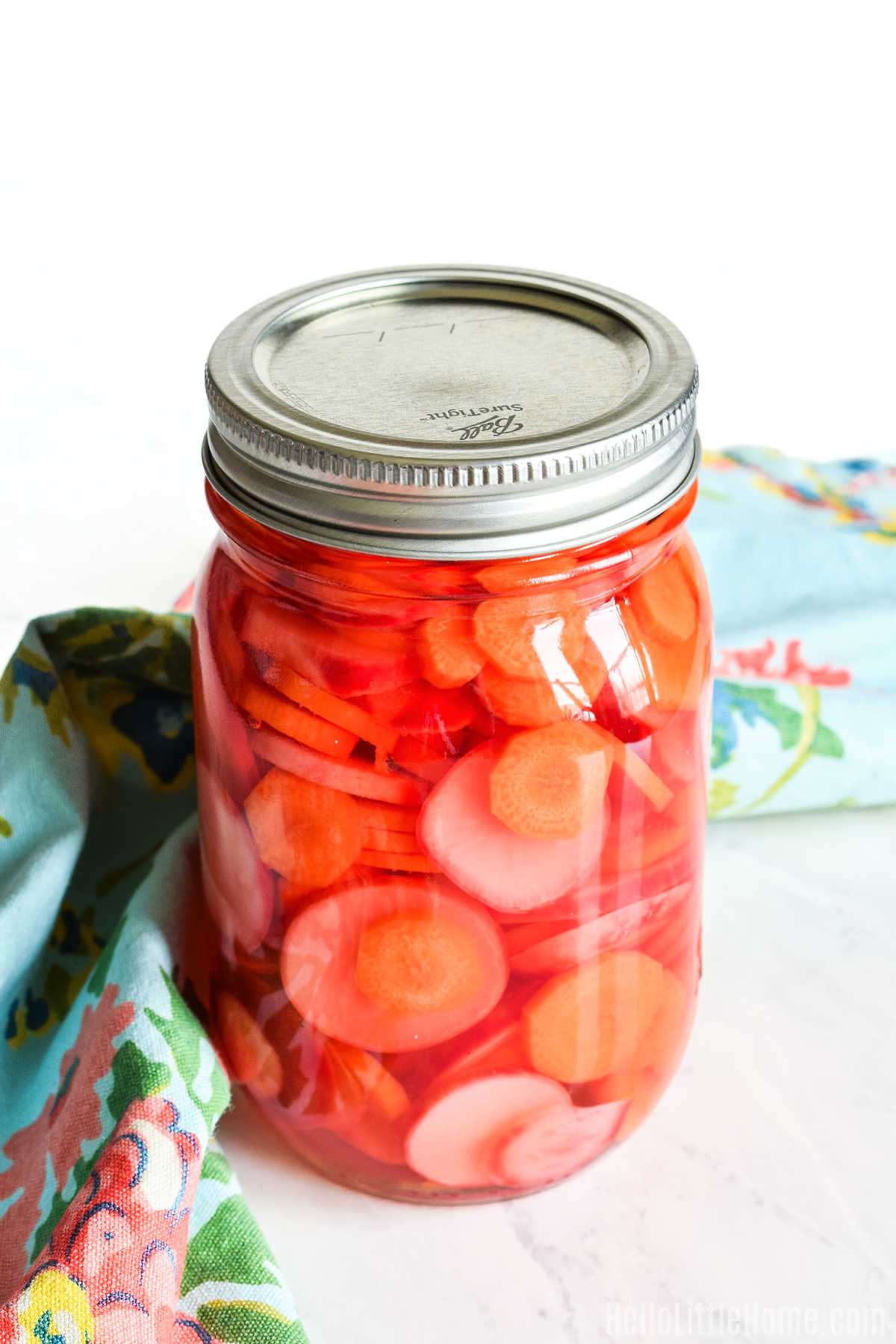 A jar of the finished pickles served with a napkin on a marble counter.
