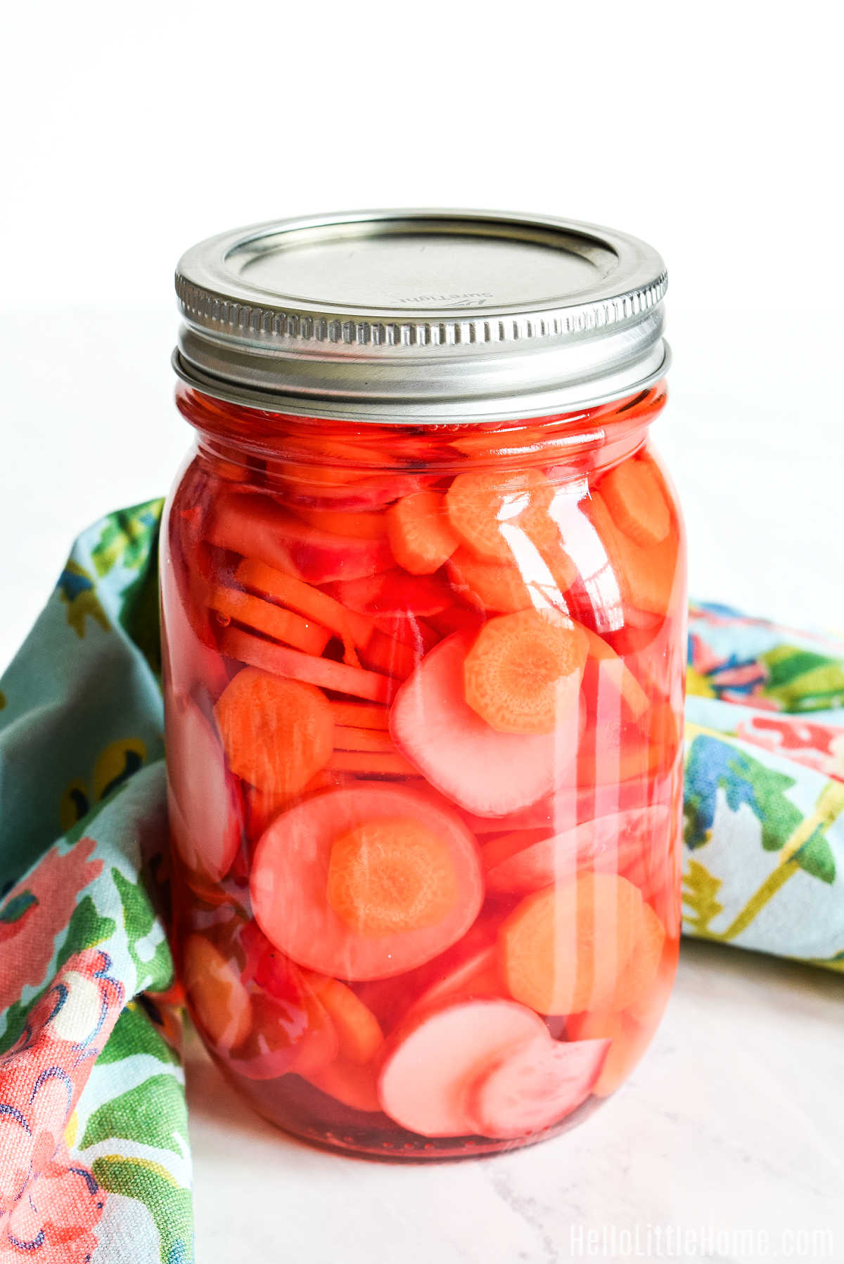 A jar of Pickled Carrots and Radishes and a napkin on a marble counter.