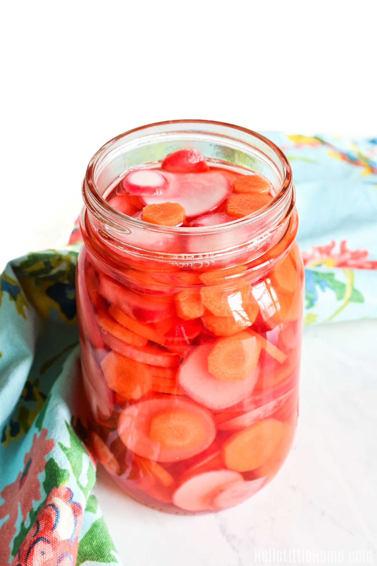 An open jar of the Radish Carrot Pickles served next to a patterned napkin.