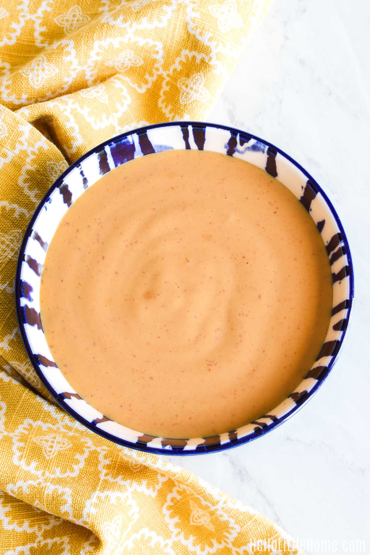 A bowl of Spicy Mayonnaise served with a yellow napkin on a marble counter.