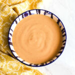 A bowl of Sriracha Mayo and a yellow napkin on a marble counter.