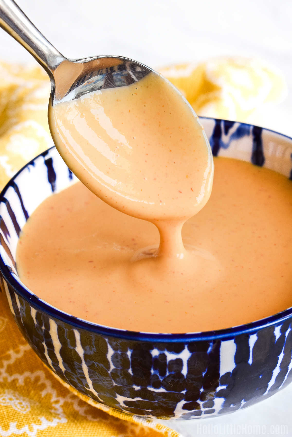 A spoon drizzling homemade Sriracha Mayo into a bowl.