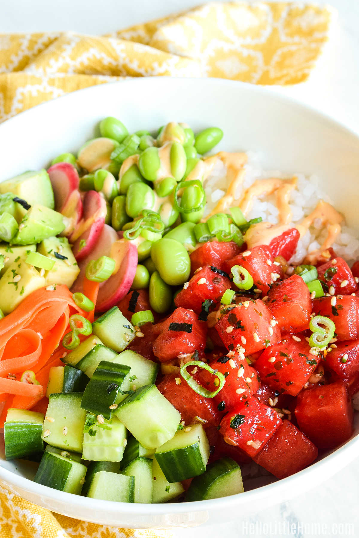 The vegan poke bowl served with a yellow napkin on a marble counter.