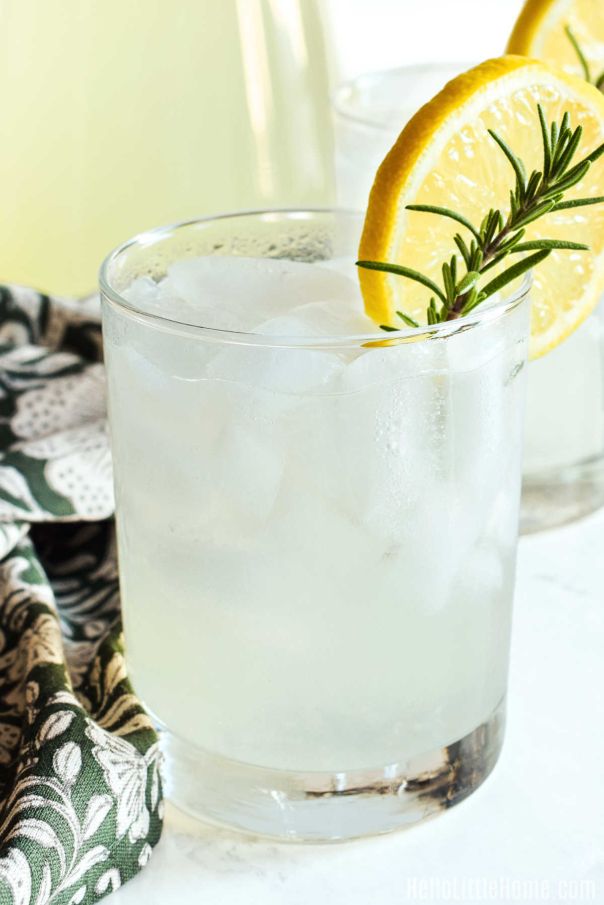 A glass of Lemonade with Rosemary and napkin on a marble counter.