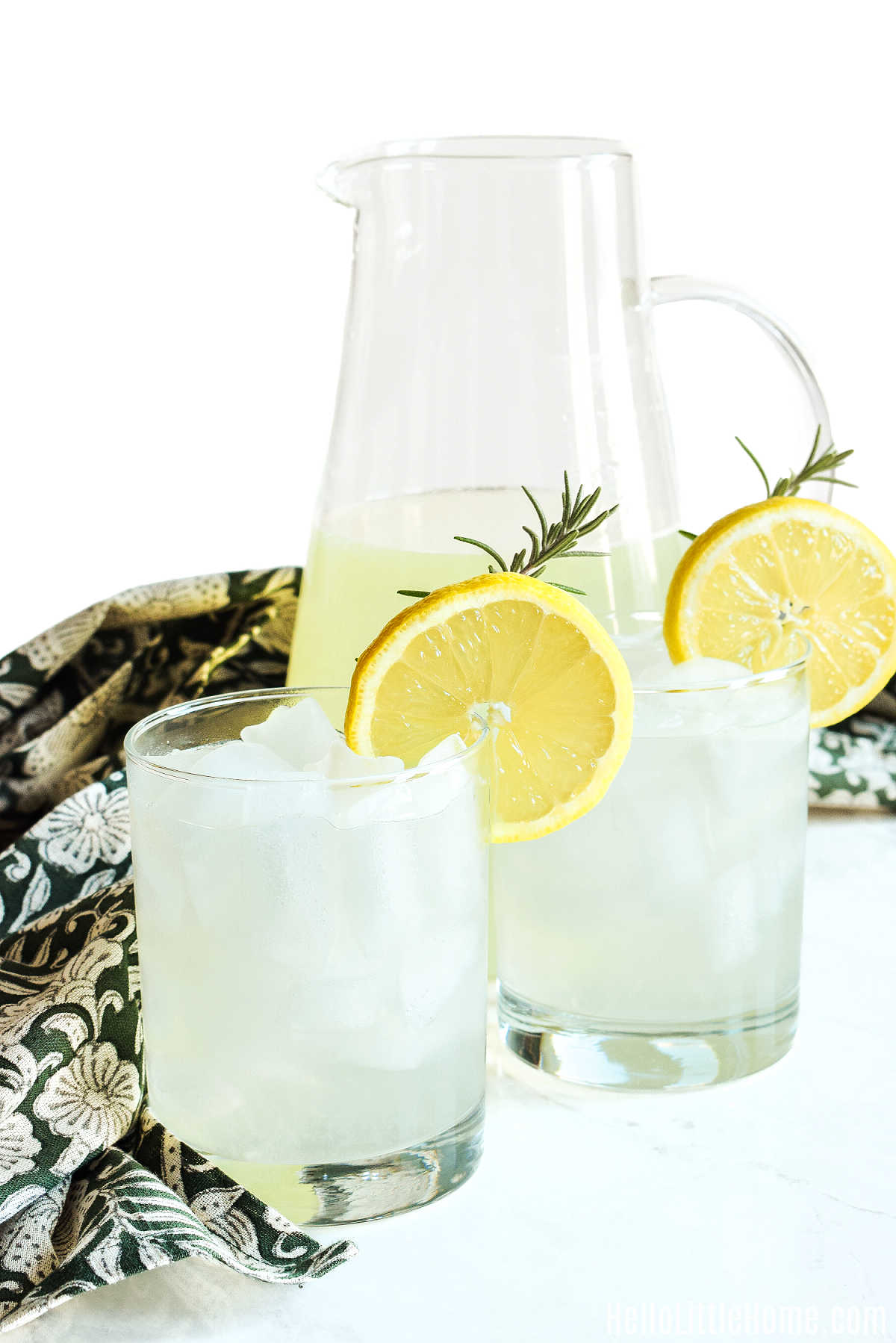 A pitcher and two glasses of lemonade on a marble counter.