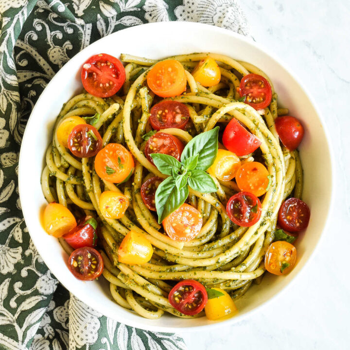 A bowl of Pesto Pasta with Tomatoes and a napkin on a marble counter.