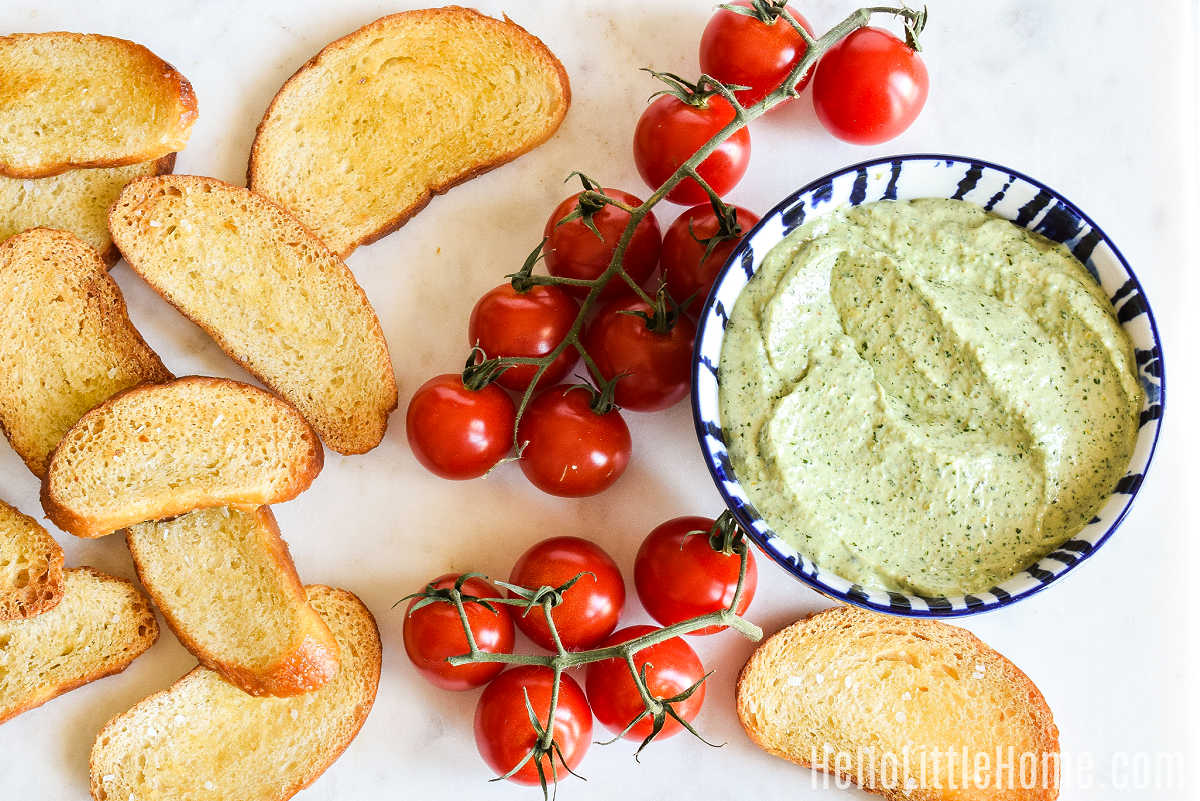 Ingredients for Ricotta Pesto Crostini arranged together on a marble counter.
