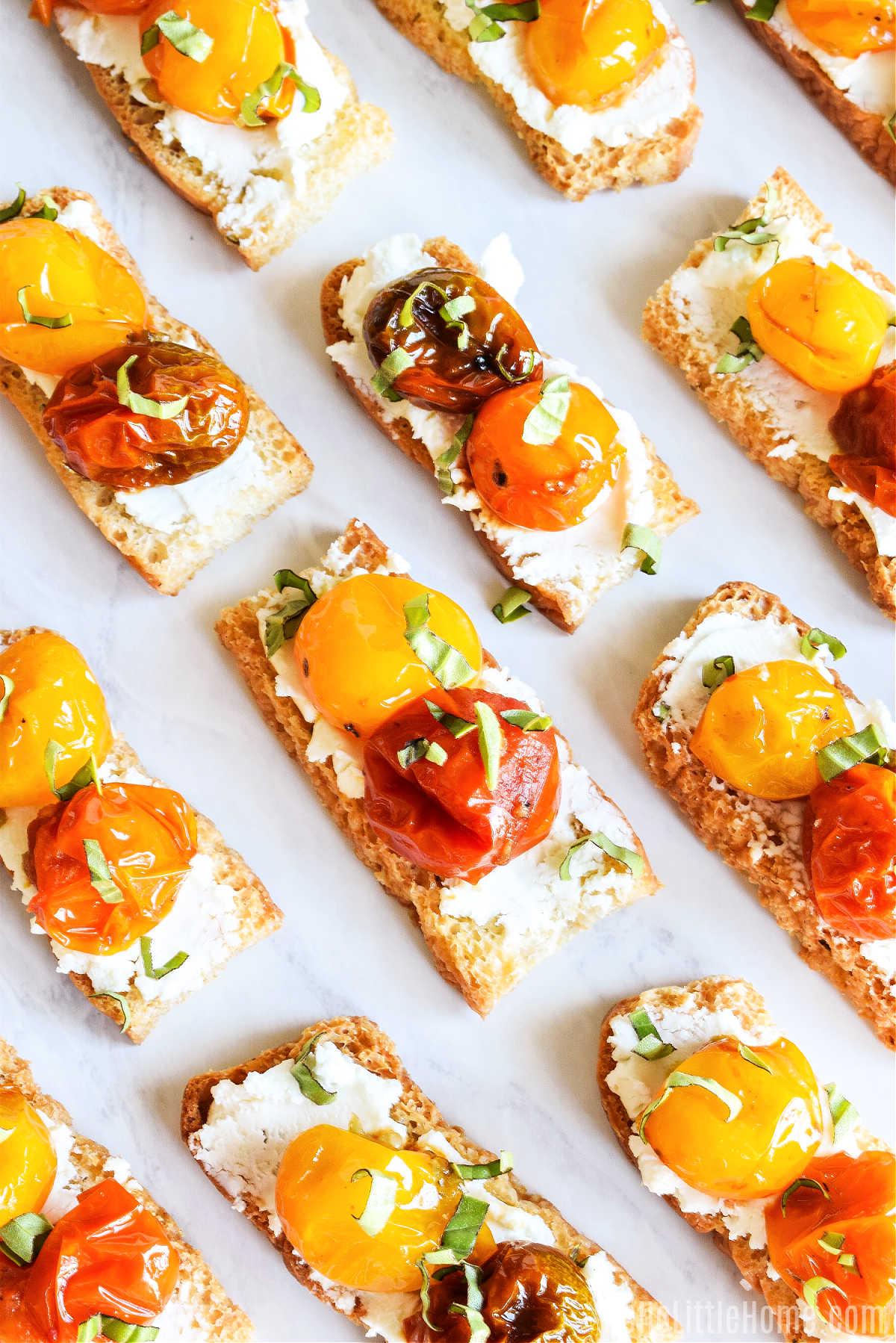 Crostini topped with goat cheese and roasted tomatoes served on a marble tray.
