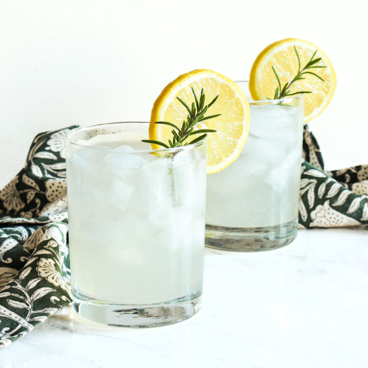 Two glasses of Rosemary Lemonade and a napkin on a marble counter.