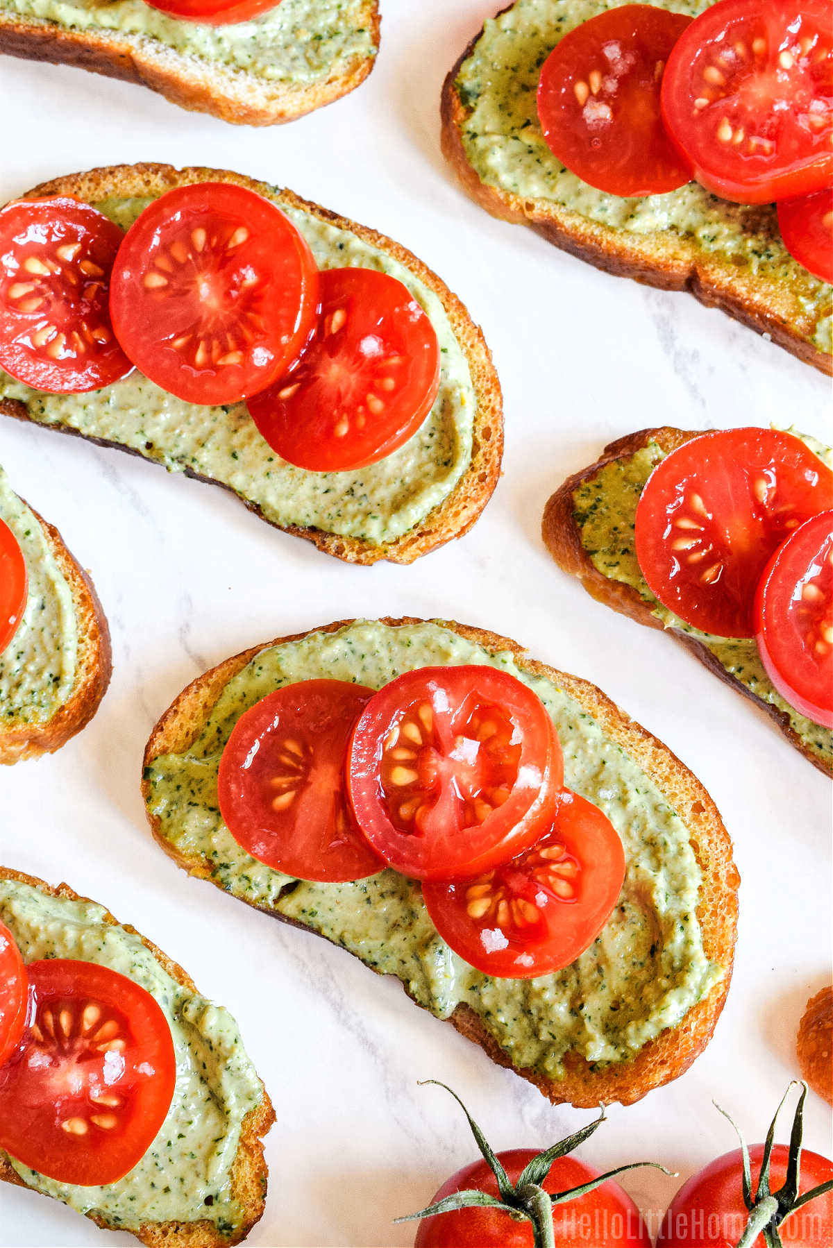 A tray of Homemade Sourdough Crostini topped with pesto ricotta and sliced tomatoes.