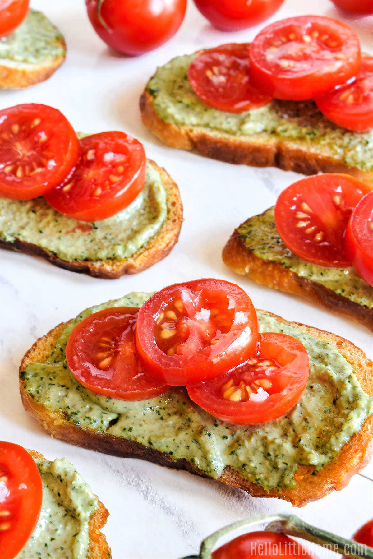 Crostini topped with cherry tomatoes and pesto ricotta on a marble tray.