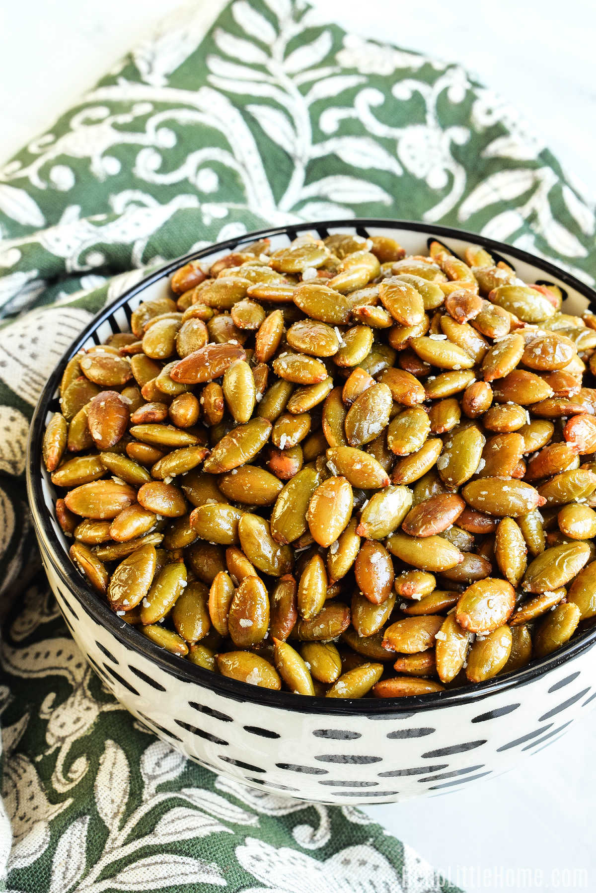 A bowl of the Baked Pepita Seeds served on a patterned napkin.